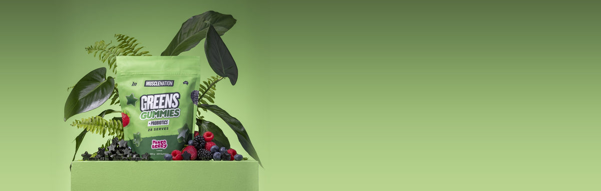 A pouch of Greens Gummies on a green plinth with leaves, berries and black star gummies