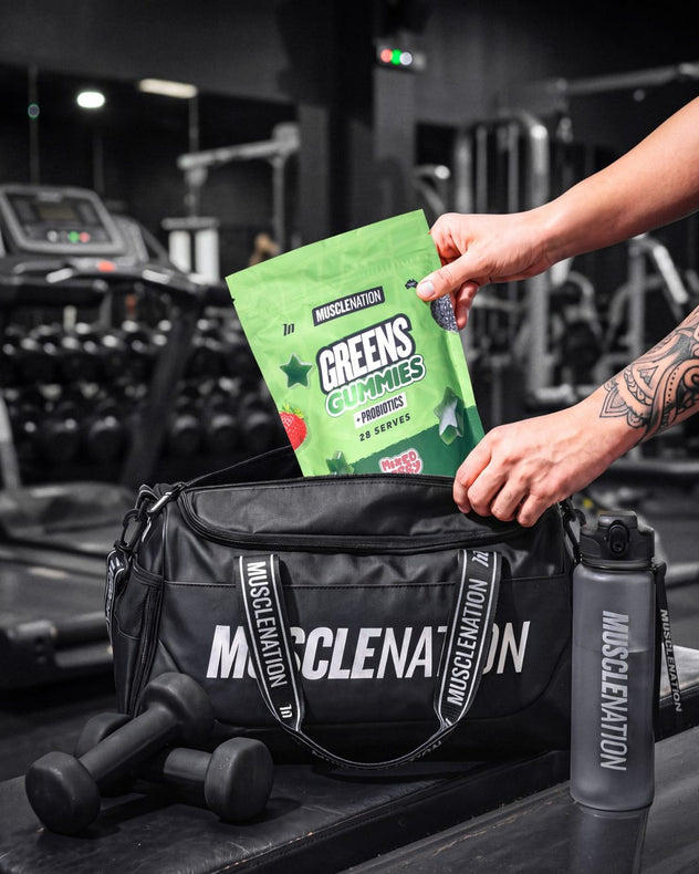 A pouch of Greens Gummies going into a Muscle Nation gym bag