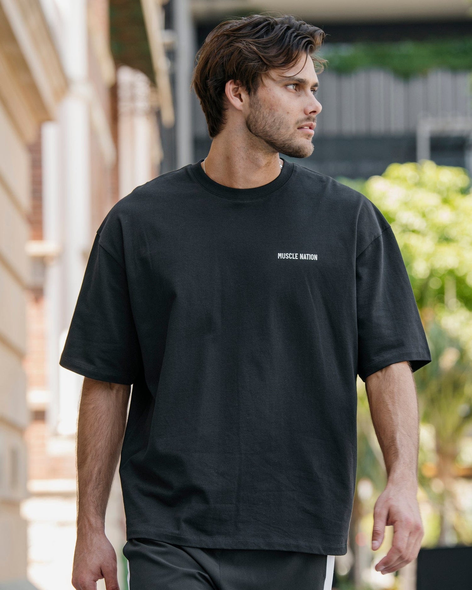 Male model wearing the black Essential Regular Fit Tee outdoors - 100% cotton crew-neck tee with Muscle Nation chest logo